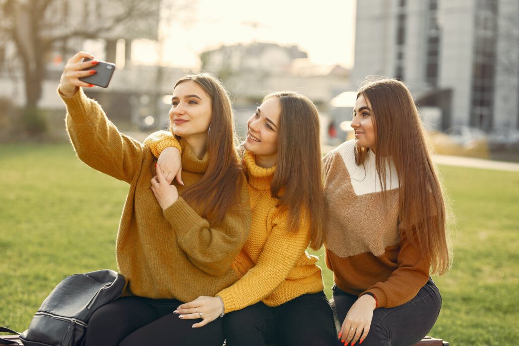 cheerful girlfriends taking selfie on smartphone in park